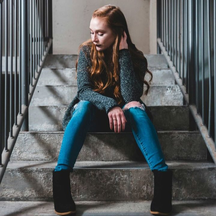 Mädchen sitzt auf Treppe - Symbolbild für selbst- und fremdgefährdende Verhaltensweisen